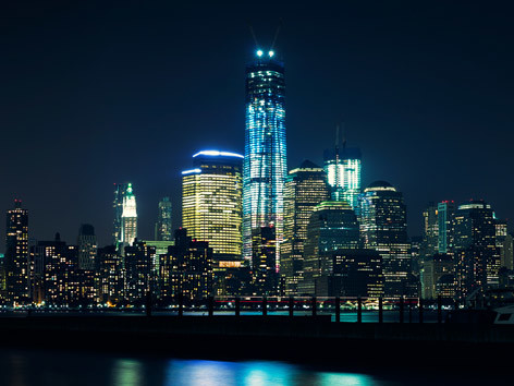Die New York Skyline bei Nacht. Der Freedom Tower strahlt bereits hell.