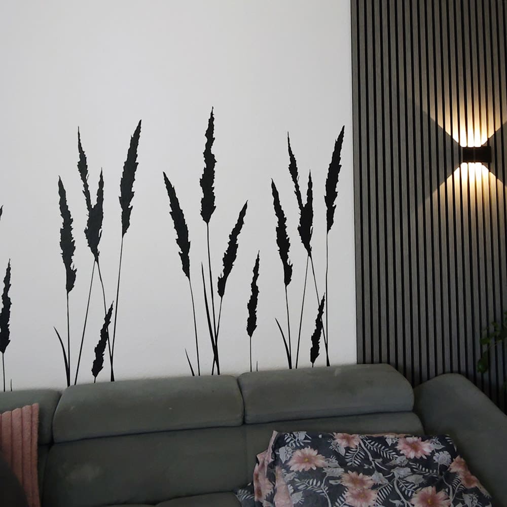 Schwarzes filigranes Schilfgras als Wandtattoo, breit angeordnet hinter einem Sofa