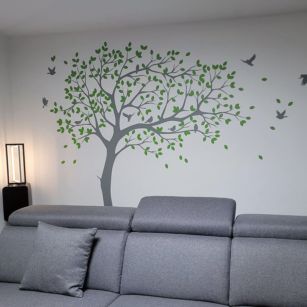 Grauer Wandtattoo-Baum mit grünen Blättern und Vögeln über einem Sofa