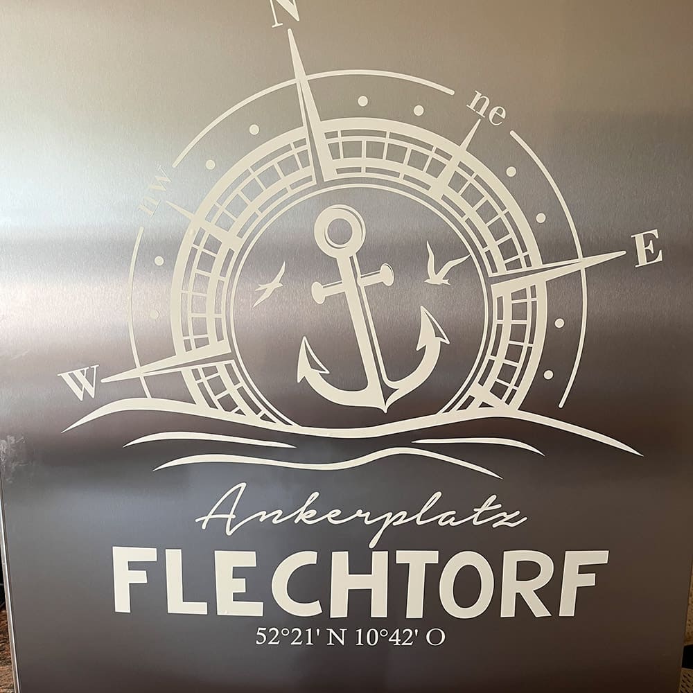 Weißes Wandtattoo mit Kompass, Anker, persönlichem Ortsnamen und Koordinaten auf dunkler Wand
