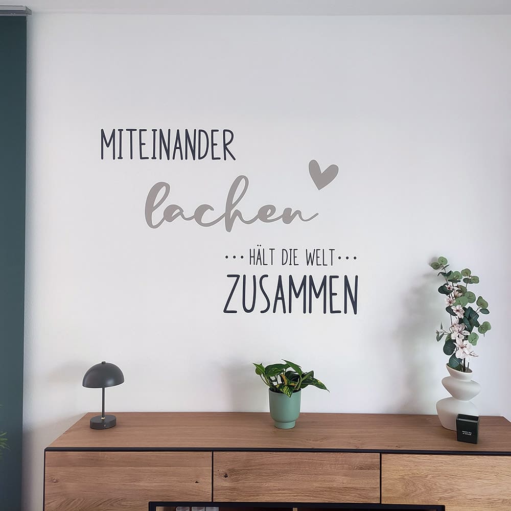 Zweifarbiges Wandtattoo Miteinander lachen über einem Holzsideboard