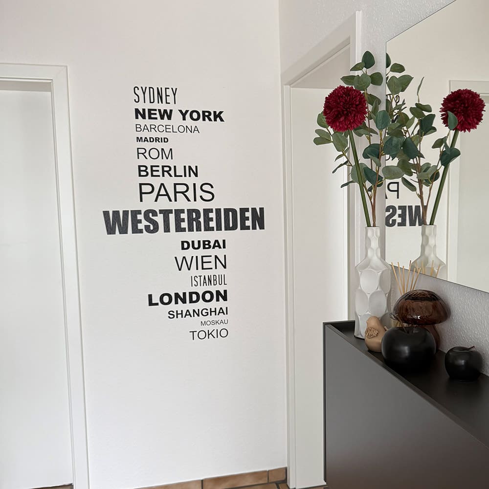 Wandtattoo mit Weltstädten und persönlichem Ortsnamen neben einem Flurspiegel