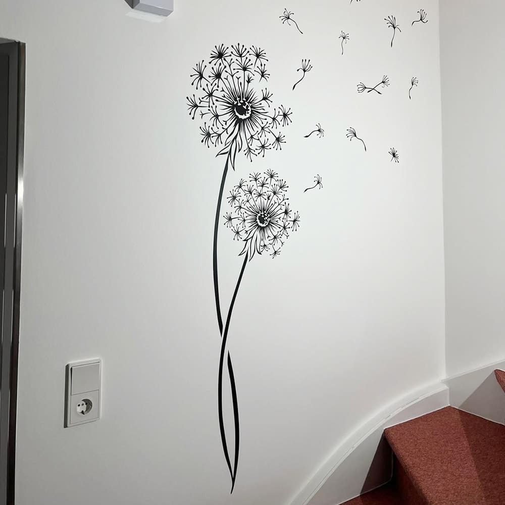 Zwei schwarze Wandtattoo-Pusteblumen mit fliegenden Schirmchen im Treppenhaus