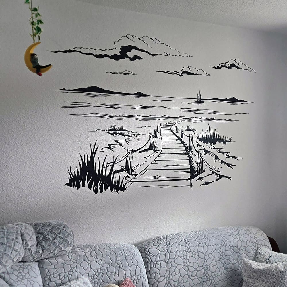 Wandtattoo Steg durch die Dünen mit Wolken und Segelboot über einem Sofa