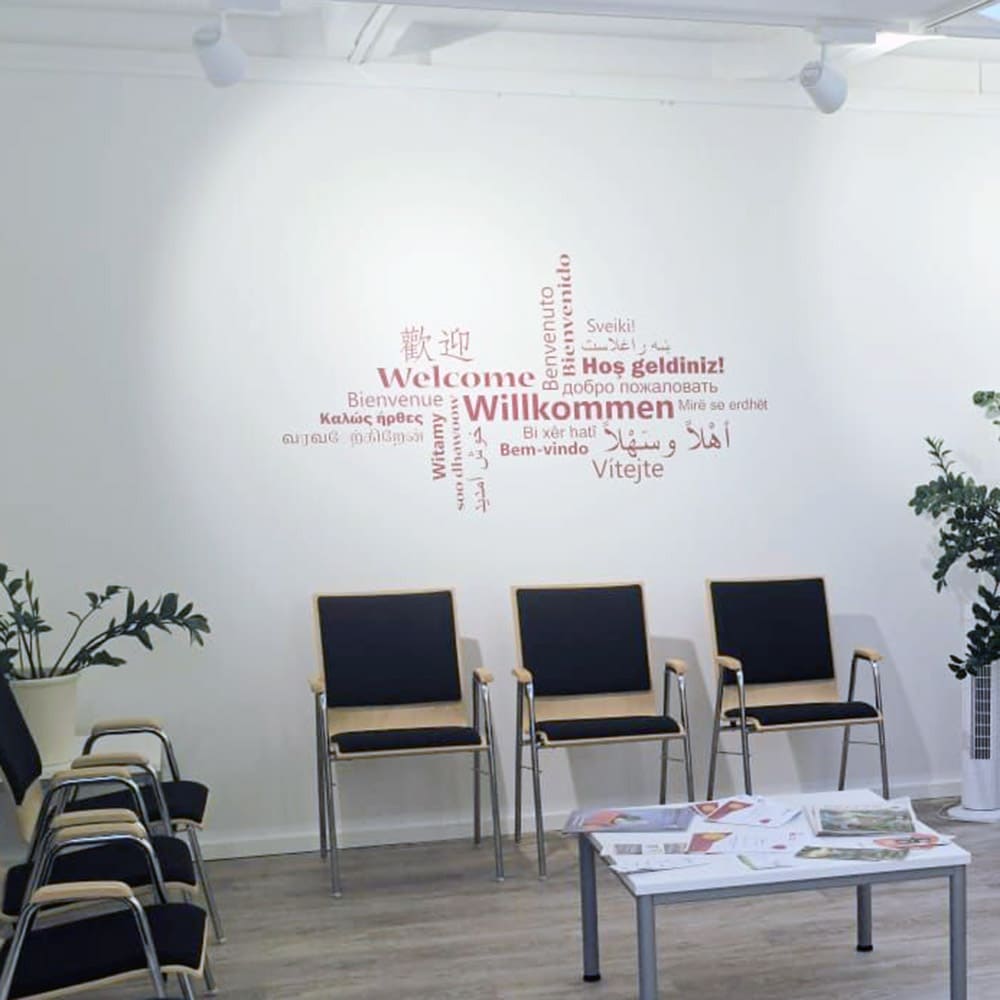 Mehrsprachiges Willkommen-Wandtattoo über Stühlen in einem hellen Empfangsbereich